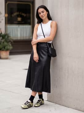 A black faux-leather midi skirt worn with a simple ribbed white tank top and a sleek leather crossbody bag for an elevated weekend brunch ensemble.