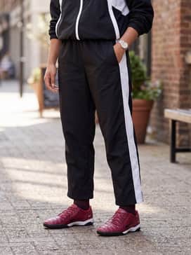 Black nylon track pants with a white side stripe and a matching zip-up windbreaker to embrace a full retro athletic aesthetic.