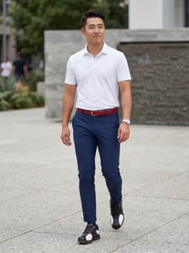 A tailored white polo shirt paired with slim-fit navy golf trousers and a coordinating red leather belt to pop the shoe's accent color.