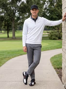 Grey tapered golf chinos worn with a crisp white quarter-zip pullover and a matching black baseball cap for a sophisticated cool-weather round.