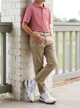 A sharp country club ensemble including a red and white striped polo shirt, khaki chino pants, and a leather belt with a silver buckle that complements the shoe's metallic stripes.