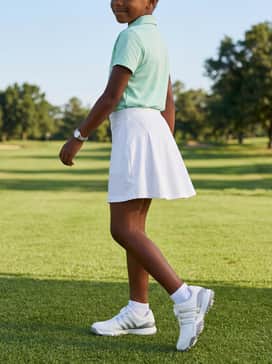 A summer-ready practice outfit with a mint green athletic top, a white pleated golf skort or performance shorts, and low-cut moisture-wicking white socks.