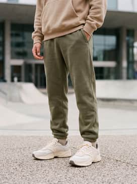 Olive green fleece joggers with a matching oversized tan hoodie and a neutral-toned baseball cap.