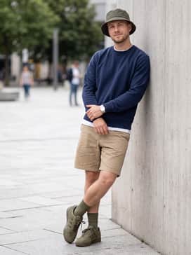 Khaki chino shorts combined with a navy blue crewneck sweater and a neutral-toned bucket hat for a relaxed weekend vibe.