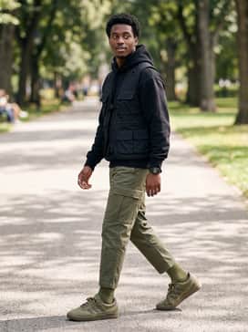 Tapered forest green cargo pants, a black heavyweight hoodie, and a technical utility vest for a modern tactical streetwear aesthetic.