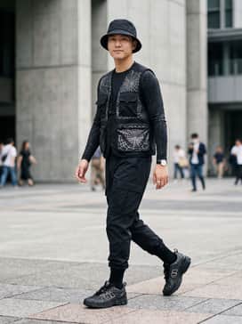 U1906f – A black techwear-inspired outfit featuring tapered cargo pants, a tactical vest over a long-sleeved compression shirt, and a waterproof bucket hat.