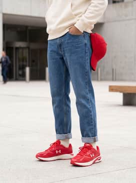 Medium-wash straight-leg denim jeans with cuffed hems, a cream-colored fleece hoodie, and a matching red baseball cap.