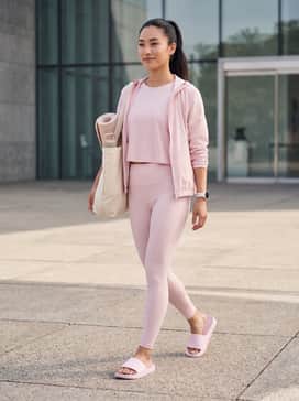High-waisted black yoga leggings paired with a matching pink cropped sports bra and an oversized white zip-up hoodie for a cohesive gym-to-street look.