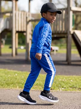 A sporty playground-ready kit with electric blue track pants featuring white side stripes, a coordinated track jacket, and a black baseball cap.