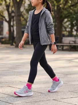 A bright pink racerback athletic tank top paired with high-waisted black moisture-wicking leggings and a lightweight grey zip-up windbreaker.