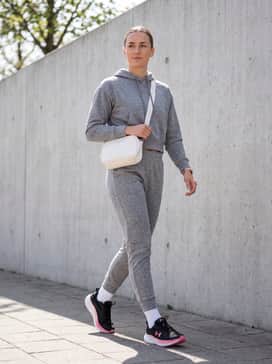 Ua Assert 11 Wide D – A grey marl tracksuit set consisting of tapered joggers and a cropped hoodie, accessorized with a white leather crossbody bag for a polished travel outfit.