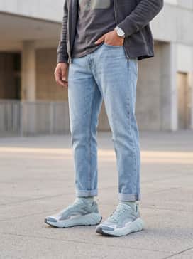 Ua Aura Ripstop – Straight-leg light-wash denim jeans with a slight cuff at the ankle, worn with a muted graphic tee and a charcoal grey zip-up hoodie for a classic street vibe.