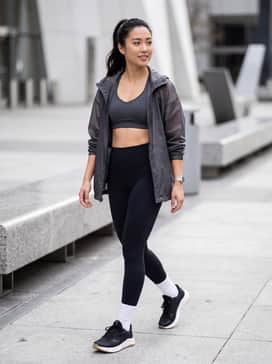 High-waisted black compression leggings paired with a charcoal grey sports bra and a translucent oversized windbreaker for a sleek, monochromatic gym-ready look.