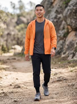 Ua Bandit Trail 3 – A performance-driven look featuring black moisture-wicking joggers, a charcoal grey compression shirt, and a lightweight orange windbreaker to echo the shoe's accents.