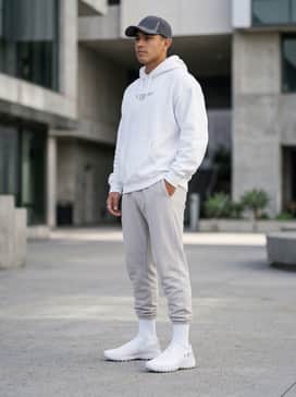 An off-duty streetwear ensemble with light-grey tapered joggers, a crisp white oversized graphic hoodie, and a charcoal grey baseball cap to match the shoe's silver accents.