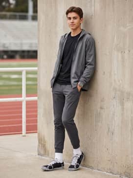 Ua Brigade Xc 2 Spikeless – A technical streetwear ensemble with slim-fit olive cargo pants, a monochromatic graphic t-shirt, and a grey windbreaker for a functional aesthetic.