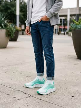 A casual school day outfit with tapered dark wash denim jeans, a white graphic tee with teal accents, and a cozy heather grey zip-up hoodie.