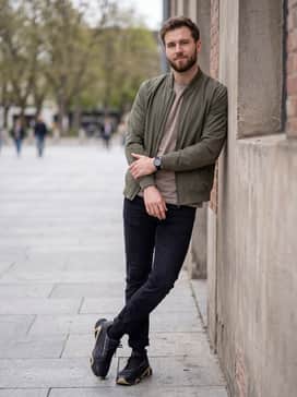 A modern streetwear outfit pairing slim-fit black tapered jeans with a neutral-toned hoodie and a lightweight technical bomber jacket for a sharp, urban aesthetic.