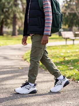 Ua Charged Rogue 6 – For younger wearers, a vibrant school-ready outfit with olive green utility joggers, a layered long-sleeve striped tee under a black puffer vest, and a sporty backpack.