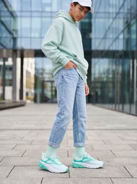 A trendy school outfit consisting of cuffed light-wash denim jeans, an oversized mint green hoodie, and a simple white baseball cap for a coordinated aesthetic.