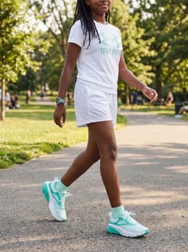 A bright summer athletic style using white mesh basketball shorts, a graphic tee with teal lettering, and a matching digital sports watch to tie the colors together.