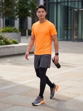A high-performance running look featuring black compression tights under charcoal grey 7-inch technical shorts, paired with a moisture-wicking neon orange tee to highlight the shoe's accents.