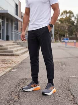 A casual streetwear ensemble with tapered black joggers, a crisp white oversized graphic t-shirt, and a grey zip-up hoodie for a balanced, neutral base.