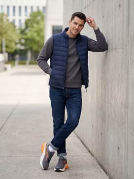 A weekend-ready outfit consisting of dark wash athletic-fit jeans, a charcoal grey crewneck sweatshirt, and a navy blue quilted puffer vest for a sporty yet rugged vibe.