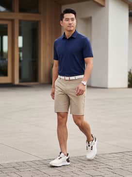 Ua Drive Fade 2 – A classic navy performance polo paired with tailored khaki technical shorts and a white leather belt for a timeless golf look.