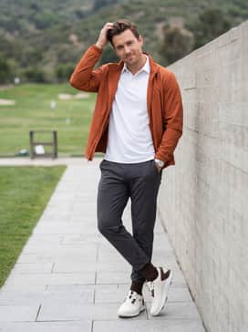 Charcoal grey tapered golf joggers and a moisture-wicking white tee topped with a burnt orange windbreaker that pulls from the shoe's small accent details.