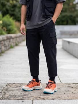 Ua Expanse Low – A streetwear-inspired outfit with oversized cream cargo pants, a black heavyweight graphic hoodie, and a techwear utility vest to lean into the Gorpcore trend.