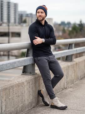 An urban commuter ensemble with tapered dark navy tech pants, a high-neck performance quarter-zip in black, and a matching orange-accented beanie.