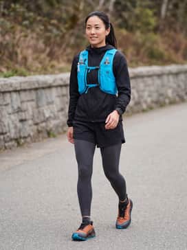 Ua Explor Trail – A performance-driven look featuring charcoal grey moisture-wicking compression leggings, a black lightweight windbreaker, and a neon blue hydration vest to echo the outsole.