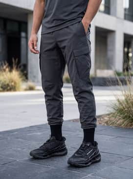A modern techwear ensemble with tapered black technical joggers, a longline black t-shirt, and an olive drab utility vest with multiple pockets for a functional urban vibe.