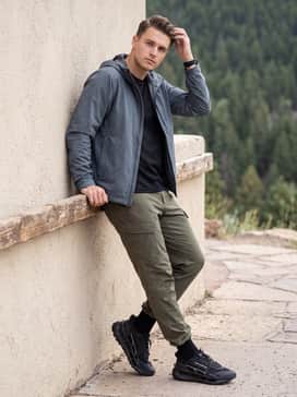 Ua Explor Trail – An outdoor hiking outfit consisting of durable olive green cargo pants, a breathable mesh base layer, and a slate grey waterproof windbreaker for unpredictable trail conditions.