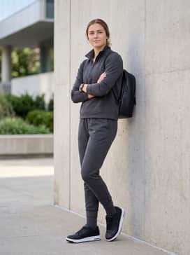 Ua Flex – Tapered charcoal grey joggers worn with a matching technical quarter-zip pullover and a minimalist leather backpack for a cohesive travel outfit.