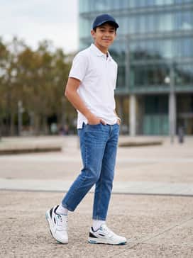 Classic light-wash tapered jeans worn with a navy blue performance polo and a matching white and blue baseball cap for a clean, preppy look.