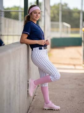 Ua Glyde Sola Tpu Jr – A high-energy game day ensemble with white pinstripe softball pants, a navy blue team jersey with pink accents, and a wide moisture-wicking headband in matching pastel pink.