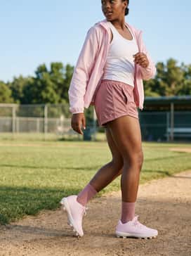 Ua Glyde Sola Tpu Jr – A coordinated pre-game warm-up look with breathable mesh athletic shorts in a dusty rose hue, a white racerback tech tank top, and a lightweight performance windbreaker.