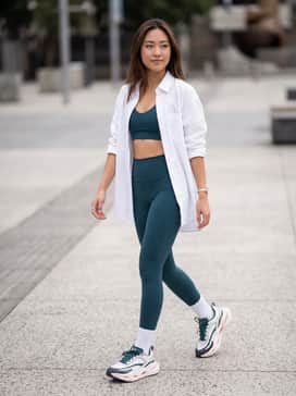 Ua Halo Racer – High-waisted dark teal leggings paired with a matching sports bra and an oversized white button-down shirt worn open for a chic gym-to-brunch look.