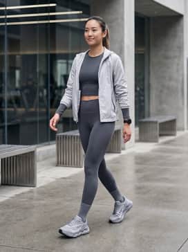 Ua Halo Runner Se – A sleek, charcoal-colored compression set consisting of high-waisted leggings and a matching long-sleeve crop top, topped with a lightweight silver windbreaker for a cohesive technical look.