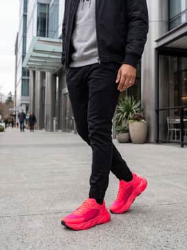 Ua Halo Trainer – A streetwear-inspired ensemble with black distressed slim-fit denim, a neutral grey graphic hoodie, and a black bomber jacket to let the neon shoes serve as the primary statement piece.
