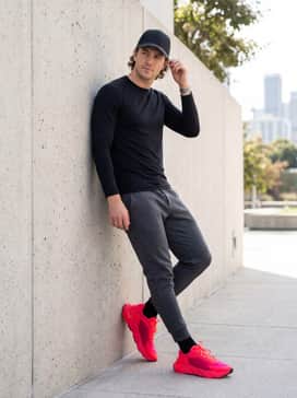 A casual athleisure outfit pairing charcoal tech-fleece joggers with a fitted black long-sleeve performance top and a sleek baseball cap for a coordinated, sporty aesthetic.