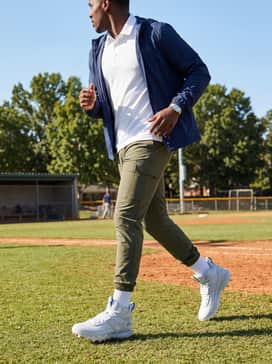 Ua Harper 10 Pro Tpu Mid – An athletic sideline ensemble featuring olive green slim-fit cargos, a crisp white moisture-wicking polo, and a lightweight navy windbreaker.