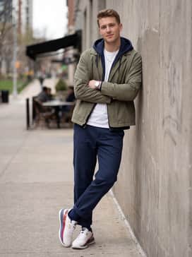 An urban streetwear outfit with olive green cargo pants, a boxy oversized navy hoodie, and subtle gold accessories that mirror the metallic Under Armour logo on the lateral strap.