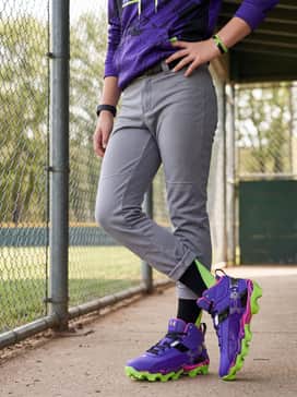 Grey tapered baseball pants with a black belt, worn with a graphic team hoodie in purple with lime green accents for a stylish pre-game warmup ensemble.
