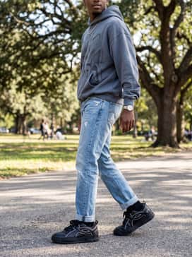 Ua Hblo – Streetwear edge featuring straight-leg distressed light-wash denim to contrast the dark shoe, paired with an oversized graphic hoodie in a neutral tone and a silver chain accessory.