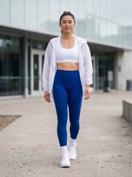 Ua Highlight Ace 2 – High-waisted compression leggings in a bold cobalt blue paired with a white sports bra and a translucent oversized windbreaker for a high-energy gym look.
