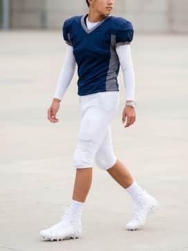 Ua Highlight Jr – Full game-day uniform consisting of matching white padded football pants, team-colored jersey, and white moisture-wicking compression sleeves.