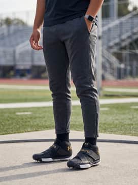 A tapered black tech-fleece tracksuit worn over a compression base layer to maintain muscle warmth during meet transitions.